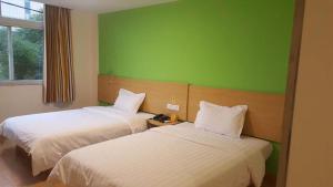 two beds in a room with a green wall at 7Days Inn Anji Centre in Huzhou