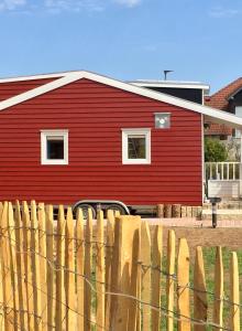 Um celeiro vermelho com uma cerca à frente. em Tinyhouse Bamberg em Pettstadt