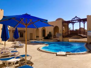 uma piscina com cadeiras e um guarda-sol azul em Cozy Family 3 BR apartment by the sea em Marsa Alam