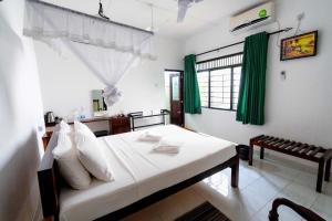 Schlafzimmer mit einem Bett mit weißer Bettwäsche und grünen Vorhängen in der Unterkunft Water Front Home Stay in Anuradhapura