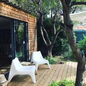 Dos sillas blancas y un árbol en el patio en 2 appartements calmes, en Fréjus