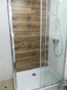 a shower with a glass door and wooden wall at Apart-noclegi in Siemiatycze