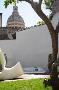 una sedia bianca seduta accanto a un muro con un albero di Iblainsuite a Ragusa