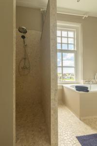 a bathroom with a shower with a tub and a window at Pastorie Stella Marie in Oudeschild