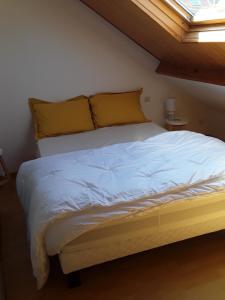a bed with white sheets and yellow pillows in a bedroom at joli duplex proche commerces et mer in Stella-Plage