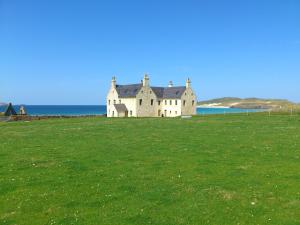 an old house in a field next to the ocean at Balnakeil House in Balnakeil