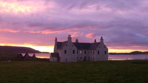 an old house in a field with a sunset at Balnakeil House in Balnakeil