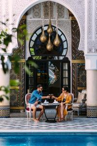 dos hombres sentados en una mesa junto a una piscina en Riad Maison Bleue and Spa, en Fez