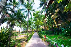 a walkway through a resort with palm trees and flowers at Hon Rom Central Beach Resort in Mui Ne