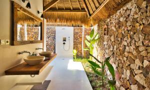 a bathroom with two sinks and a stone wall at Segara Lombok Beach Resort in Selong Belanak