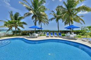uma piscina com palmeiras, cadeiras e guarda-sóis em Maxwell Beach Villas em Christ Church