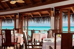 a restaurant with white tables and chairs and the ocean at Anantara Dhigu Maldives Resort in South Male Atoll