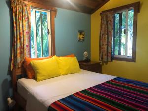 a bedroom with a bed with yellow pillows and windows at Colinda Cabanas in Caye Caulker