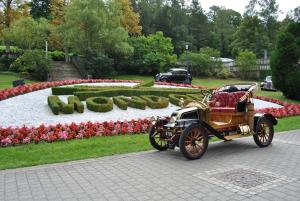 stary samochód zaparkowany przed ogrodem pełnym kwiatów w obiekcie Mondorf Parc Hotel & Spa w mieście Mondorf-les-Bains