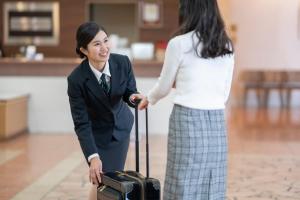 a woman is shaking hands with a woman with a suitcase at Hotel Econo Yokkaichi in Yokkaichi