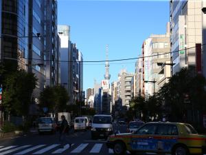 una persona cruzando una concurrida calle de la ciudad con coches y un taxi en APA Hotel Kodemmacho-ekimae, en Tokio