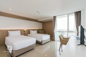a hotel room with two beds and a desk at Rattanachol Hotel in Chon Buri