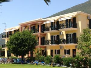 a large yellow building with balconies and a tree at Bayside Apartments in Vasiliki