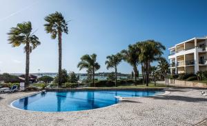 Una piscina con palmeras y un edificio. en Clube Alvor Ria - Prime Residence, en Alvor
