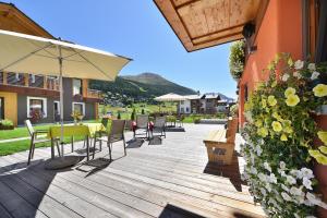 une terrasse en bois avec une table, des chaises et un parasol dans l'établissement Hotel Roberta Alpine Adults only, à Livigno