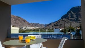 een tafel met een glas sinaasappelsap op een balkon met bergen bij El Guanche A in Valle Gran Rey