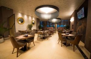 ein Restaurant mit Tischen und Stühlen und einem großen Kronleuchter in der Unterkunft Maya Luxury Alezzi Beach Resort in Mamaia Nord – Năvodari