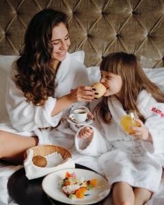 a woman and a little girl sitting on a bed eating food at Hotel Resort&Spa Kamelot in Kamenitsa