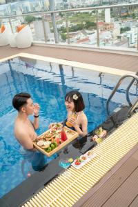 a man and woman in a swimming pool with a tray of food at Roliva Hotel & Apartment Danang in Da Nang