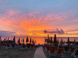 eine Gruppe von Stühlen und Sonnenschirmen am Strand bei Sonnenuntergang in der Unterkunft Piccolo Paradiso in Albenga