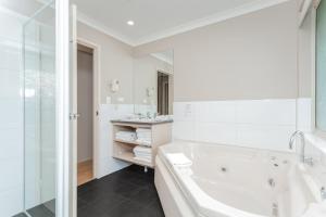 a white bath tub sitting next to a white sink at Quality Apartments Banksia Gardens in Albany