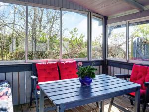 4 person holiday home in HAMBURGSUND في هامبورغسوند: شرفة مع طاولة خشبية وكراسي حمراء