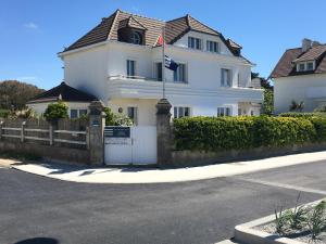 une grande maison blanche avec une clôture et un portail dans l'établissement La Villa plein vent "Lumière du Cap" vue mer, à Barneville-Carteret