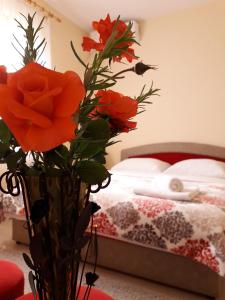 a vase with flowers in front of a bed at Apartmani Sara Trebinje in Trebinje