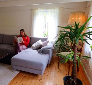 a woman sitting on a couch reading a book in a living room at Det Hvite Hus in Feda
