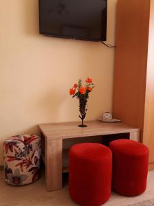 a table with a vase of flowers and two red stools at Apartmani Sara Trebinje in Trebinje