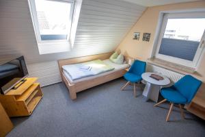 a small room with a bed and two blue chairs at Hotel Pension Nordseewelle in Norddeich