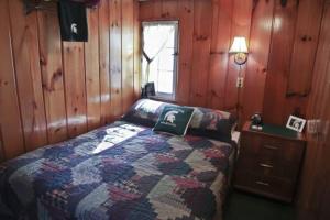 1 dormitorio con 1 cama y pared de madera en Cabin #1 - Cedar Village cabin en Carp Lake