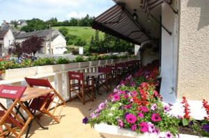 eine Außenterrasse mit Tischen, Stühlen und Blumen in der Unterkunft Logis Hotel Du Commerce in Pont-d'Ouilly