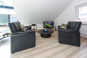 2 schwarze Ledersessel in einem Wohnzimmer mit einem TV in der Unterkunft Jever-Ferienhaus Himmelsblick in Jever