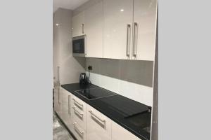 uma cozinha com armários brancos e um balcão preto em Bright, stylish Studio flat with Sky Sports em Earley