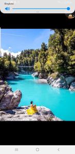 a person sitting on a rock in front of a river at The Blackhouse Cottage in Hokitika