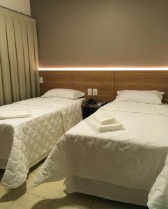 two beds in a hotel room with white sheets at Hotel Alpha in Uberlândia