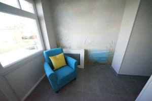 a blue chair with a yellow pillow sitting next to a window at Residenz Strandläufer in Wenningstedt