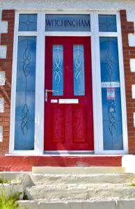 a red door on a brick building with two windows at Witchingham B&B in Holyhead