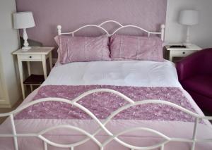 a bed with a white frame and purple sheets and pillows at Witchingham B&B in Holyhead