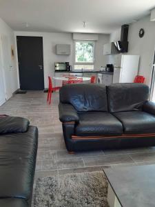 a living room with a black leather couch and a kitchen at Gîte les 2 pins - Audenge in Audenge