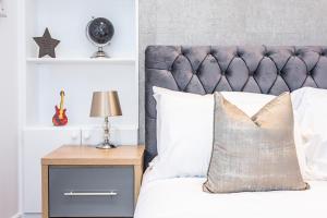 ein Bett mit einem grauen Kopfteil und einem hölzernen Nachttisch mit einer Lampe in der Unterkunft Cozy and Serene brand-new flat in Kilburn, London in London