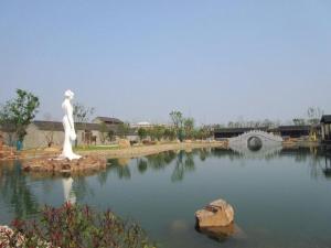 a statue in the middle of a pond with a bridge at 7Days Premium Suqian Yanghe Town Branch in Suqian