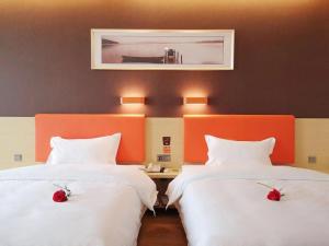 Dos camas en una habitación de hotel con flores rojas. en 7Days Premium Heze Train Station Branch, en Heze
