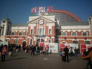 un grupo de personas de pie fuera de un edificio con un reloj en 7 Days Hotel Shenyang Railway Station Zhongshan Square Branch en Shenyang